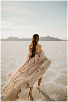 a woman in a dress walking on the beach with her back turned to the camera