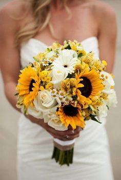 a bride holding a bouquet of sunflowers and other flowers on her wedding day