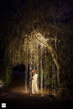 a bride and groom standing under an archway covered in fairy lights