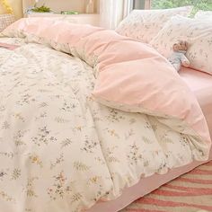 a bed with pink comforter and pillows in a room next to a large window