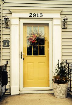 a yellow front door with two potted plants on the side and number 2095