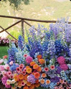 an arrangement of colorful flowers in a pot on the ground near a fence and grass area