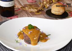 a white plate topped with meat covered in gravy next to a bottle of wine