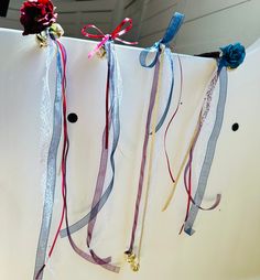 three ribbons are hanging from the side of a refrigerator with bells attached to it and flowers on top