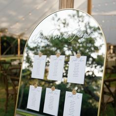 a mirror with seating cards on it in the middle of a table at a wedding