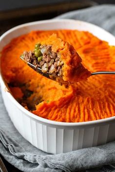 a spoon full of mashed potatoes with meat and vegetables in it, being lifted from a casserole dish