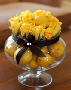 a glass bowl filled with yellow roses and lemons on top of a wooden table