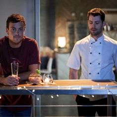 two men sitting at a table with food and drinks in front of them on the counter