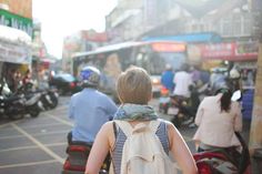 a woman is walking down the street with her back turned to the camera and people on scooters behind her