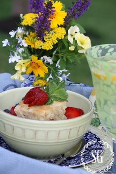 a bowl filled with cake and strawberries on top of a blue table cloth next to a glass of water