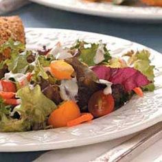 a white plate topped with a salad covered in lettuce and carrots next to a slice of bread