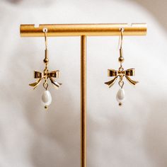 dainty pearl drop bow earrings inspired by Amy March from Little Women MATERIALS: -glass beads -gold plated brass bow charms -Earring Hooks are 18k Gold Plated Stainless Steel + Nickel Free -Brass Huggie Hoop Earrings are 18k Gold Plated + Nickel Free -Studs are 18k Gold Plated 304 Stainless Steel with 316 Surgical Stainless Steel Pin JEWELRY CARE: -avoid contact with perfume, body lotions, or other chemicals. -remove jewelry when swimming + bathing -store in a cool dry place As always, feel free to message me with any questions! -Holly Gold Pearl Earrings With Bow For Gift, Gold Pearl Earrings With Bow As Gift, Academia Accessories, Amy March, Brass Bow, Earth Style, Body Lotions, Jewelry Pearl, Bow Jewelry