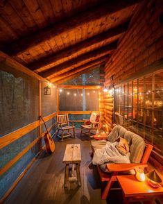 a porch with wooden furniture and string lights on the ceiling is lit up at night