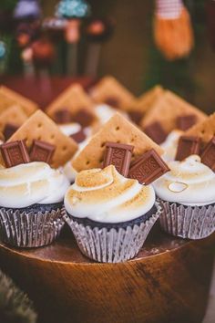 cupcakes with white frosting and chocolate on top are arranged in a wooden bowl