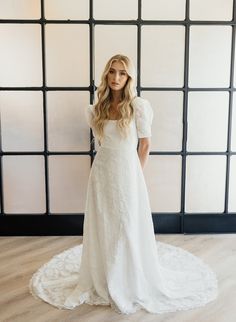 a woman standing in front of a wall wearing a white wedding dress with short sleeves