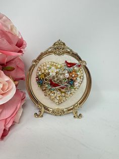 a close up of a brooch on a table with flowers in front of it