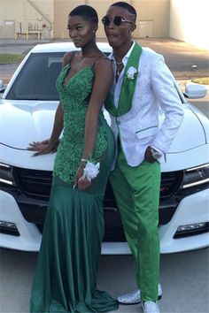 two people standing next to a white car in front of a building with a green dress on