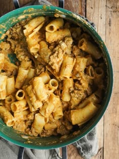 a green pot filled with pasta and meat on top of a wooden table next to a gray towel