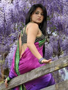 a woman in a purple dress standing on a wooden rail next to some purple flowers