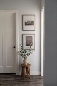 a vase with flowers is sitting on a stool in front of a white door and framed pictures