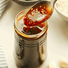 a spoon full of sauce sitting on top of a jar