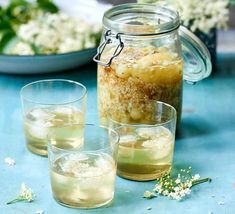 three glasses filled with liquid sitting on top of a table next to plates and flowers