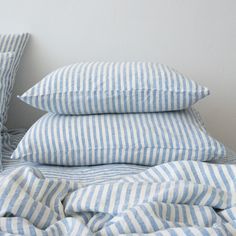 three pillows are stacked on top of each other in front of a bed with blue and white striped sheets