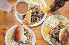 three plates with pulled pork sandwiches, coleslaw, and pickles on them