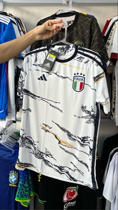 a person holding up a soccer jersey in front of other shirts on display at a store