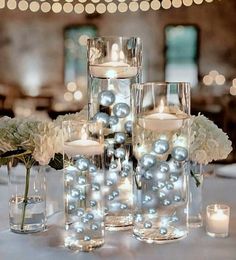 candles and flowers are arranged in vases on a table with lights behind them at a wedding reception