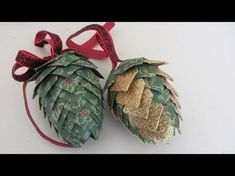 two pine cones decorated with gold glitters and red ribbon hanging on a white wall