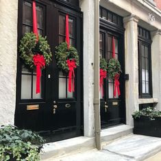 two black doors decorated with wreaths and red ribbon on the side of a building