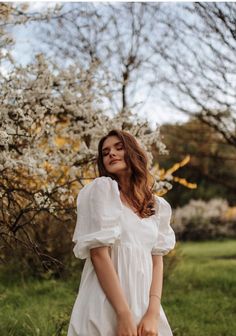 a woman in a white dress standing next to a tree