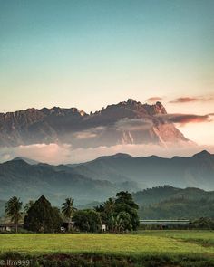 the mountains are covered in clouds and green grass as the sun is setting behind them