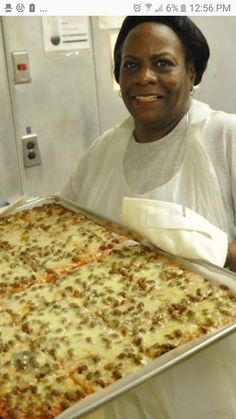 a woman holding up a large pan of pizza