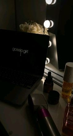 an open laptop computer sitting on top of a desk next to bottles and candles in front of a mirror