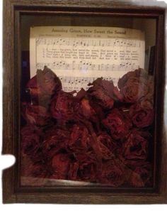 an old sheet music with red roses in a wooden frame on top of musical notes