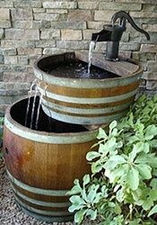 two wooden barrels with water running from them in front of a brick wall and green plants