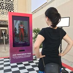 a woman standing in front of a sign with her back to the camera and looking at something