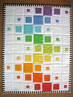 a quilted wall hanging with squares and lines on the bottom, in different colors