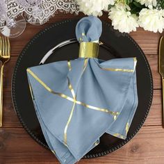 a black plate topped with a blue napkin and gold trimmings next to silverware