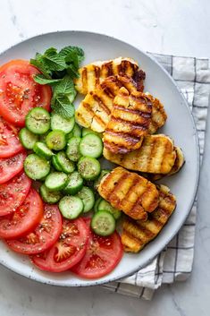 grilled chicken, sliced cucumbers and tomatoes on a white plate