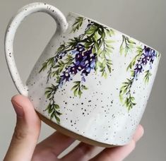 a hand holding a white coffee cup with purple flowers on the outside and green leaves on the inside