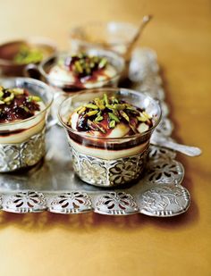 four desserts are sitting on a silver serving tray with spoons and napkins