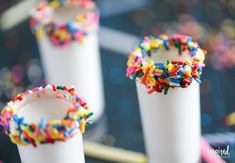 three white cups filled with sprinkles on top of a table