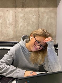 a woman sitting at a desk with a laptop computer in front of her face and wearing glasses