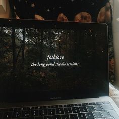 an open laptop computer sitting on top of a desk next to a window with the words folklore written on it