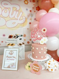 a pink and white cake sitting on top of a table next to balloons, flowers and signs