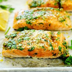 two salmon fillets on a baking sheet with parmesan cheese and lemon wedges