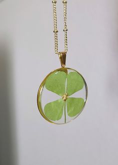 a green four leaf clover necklace hanging from a gold plated chain on a white wall